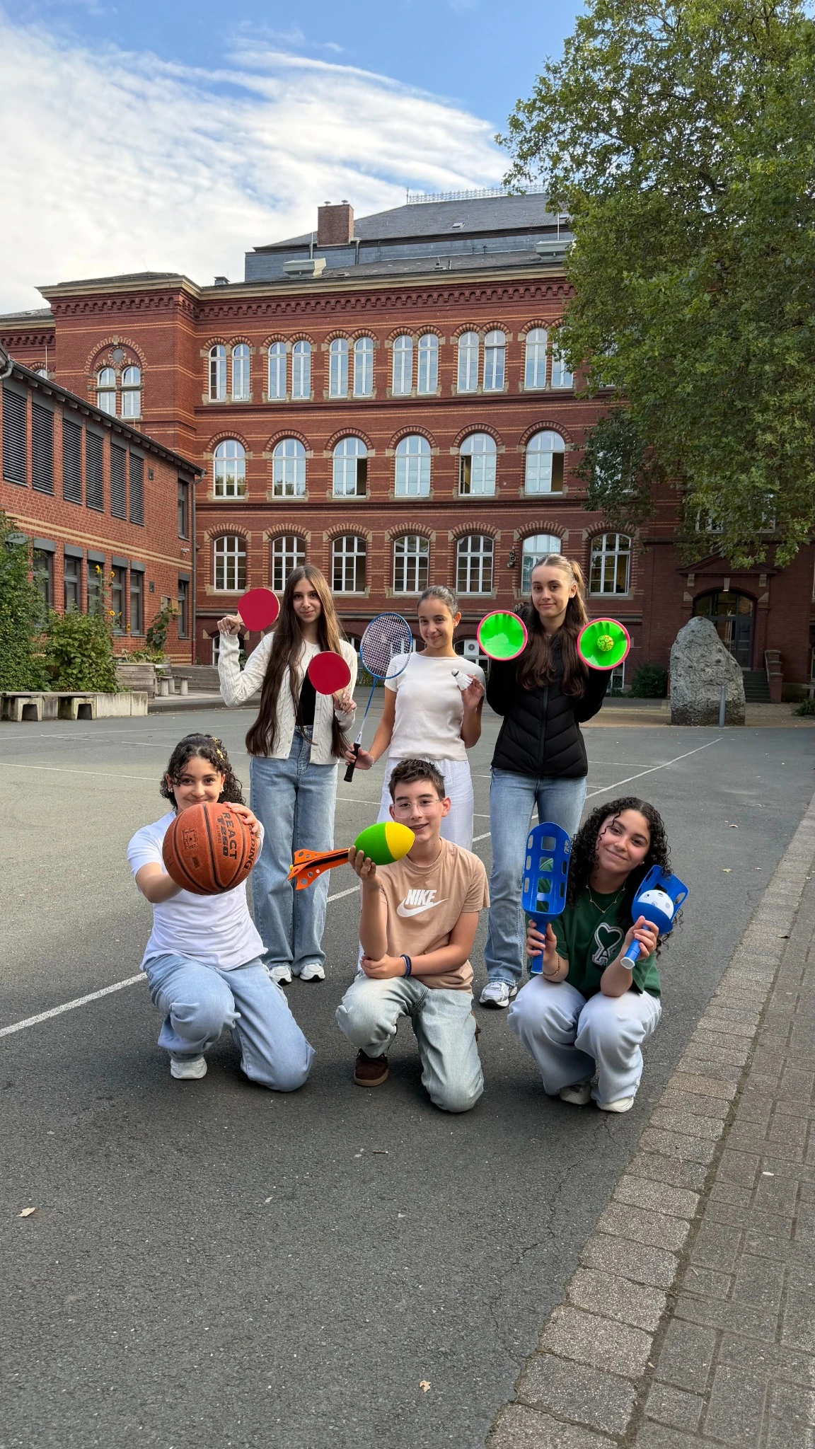 Schülerinnen und Schüler zeigen auf dem HvH-Schulhof Bälle, Schläger und weitere Spielgeräte.